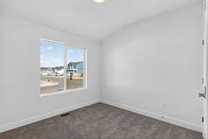 Spare room featuring vaulted ceiling and dark carpet