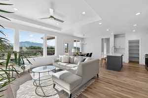 Living area featuring a mountain view, ceiling fan, light wood-style floors, hanging lights, and a tray ceiling