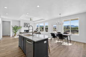 Kitchen featuring an island with sink, ceiling fan, light stone countertops, a raised ceiling, and a mountain view