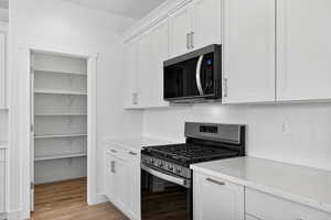 Kitchen with stainless steel appliances, white cabinetry, and light wood-style flooring