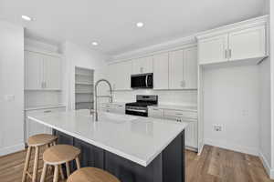 Two tone kitchen with stainless steel range oven, a breakfast bar area, two tone cabinets, a center island with sink, and tasteful backsplash