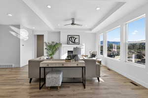 Home office featuring a raised ceiling, light wood-style flooring, ceiling fan, a mountain view, and recessed lighting