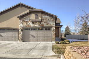 View of front of property featuring stone siding, concrete driveway, and stucco siding