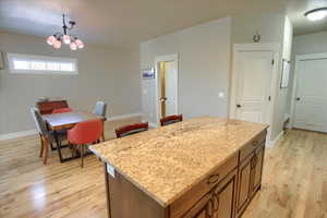 Kitchen featuring hanging light fixtures, light wood finished floors, light stone counters, and a chandelier