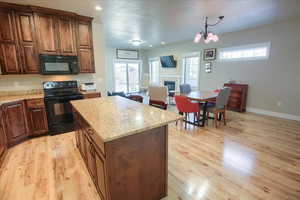 Kitchen with black appliances, a glass covered fireplace, a center island, hanging light fixtures, and light wood-type flooring