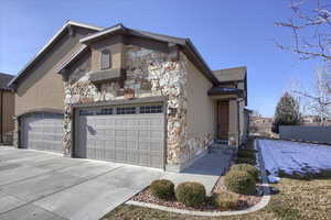 View of front of house with stone siding, driveway, and stucco siding
