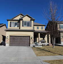 View of front facade with stone siding, stucco siding, an attached garage, and covered porch