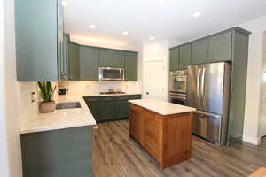 Kitchen featuring stainless steel appliances, green cabinetry, light stone countertops, backsplash, and dark wood-type flooring