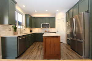Kitchen featuring green cabinets, stainless steel appliances, a center island, light stone countertops, and dark wood-style floors