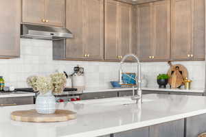 Kitchen with under cabinet range hood, decorative backsplash, gas range, and light stone countertops