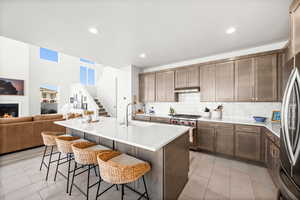 Kitchen featuring stainless steel appliances, a breakfast bar area, a kitchen island with sink, open floor plan, and light stone counters