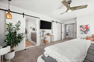 Master bedroom featuring a barn door, carpet floors, ensuite bath, and a ceiling fan