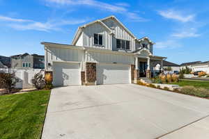 View of front facade with covered porch, board and batten siding, concrete driveway, an attached garage, and stone siding