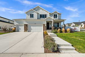 View of front facade with covered porch, concrete driveway, board and batten siding, stone siding, and a garage