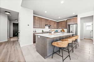 Kitchen with a kitchen breakfast bar, a center island with sink, dark brown cabinetry, light tile patterned floors, and light stone countertops