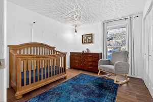 Bedroom featuring a crib, wood finished floors, a closet, and a textured ceiling