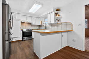Kitchen featuring white cabinets, a peninsula, tasteful backsplash, stainless steel appliances, and open shelves