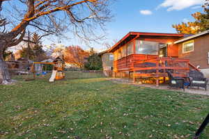 Fenced backyard featuring a sunroom, a playground, and a deck