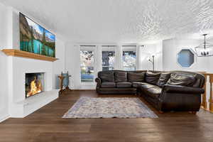 Living area with a fireplace, dark wood-type flooring, a textured ceiling, and a chandelier