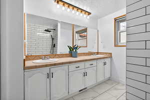 Full bath featuring double vanity, a textured ceiling, light marble finish floors, a tile shower, and track lighting