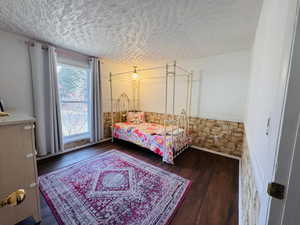 Bedroom with a wainscoted wall, a textured ceiling, and dark wood-style flooring