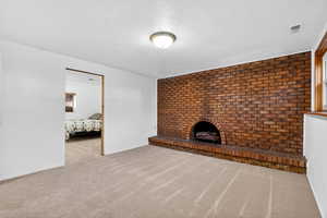 Unfurnished living room with light carpet, a textured ceiling, brick wall, and a fireplace