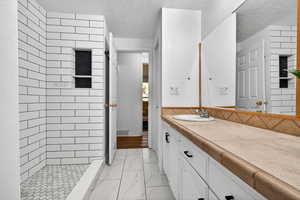 Full bathroom with light marble finish floors, vanity, a tile shower, and a textured ceiling