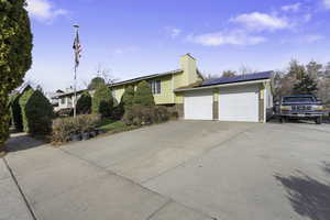 View of front of house featuring solar panels, driveway, brick siding, a chimney, and an attached garage