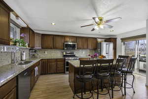 Kitchen with stainless steel appliances, a breakfast bar, a kitchen island, light stone countertops, and light wood finished floors