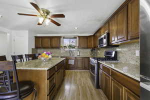 Kitchen with a breakfast bar, stainless steel appliances, light stone countertops, brown cabinetry, and recessed lighting