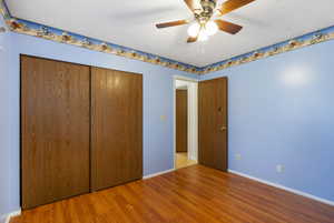 Unfurnished bedroom with wood finished floors, a closet, and a ceiling fan