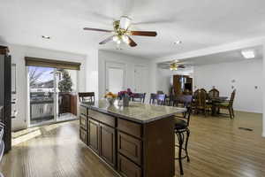 Kitchen with a kitchen bar, light stone counters, light wood finished floors, a kitchen island, and recessed lighting