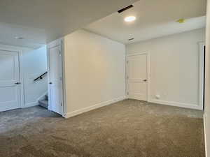 Carpeted spare room featuring stairs and baseboards