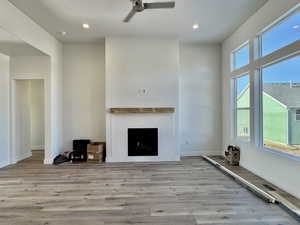 Unfurnished living room featuring recessed lighting, a fireplace, ceiling fan, wood finished floors, and a high ceiling