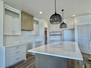 Kitchen with white cabinets, a kitchen island with sink, light stone counters, glass insert cabinets, and hanging light fixtures