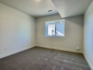 Spare room featuring dark carpet and a textured ceiling
