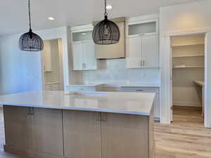Kitchen featuring decorative light fixtures, glass insert cabinets, backsplash, white cabinets, and recessed lighting