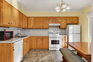 Kitchen with white appliances, backsplash, light countertops, pendant lighting, and stone finish floors