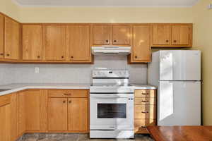 Kitchen featuring white appliances, light countertops, under cabinet range hood, brown cabinetry, and decorative backsplash