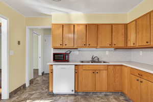 Kitchen featuring dishwasher, light countertops, backsplash, brown cabinetry, and ornamental molding