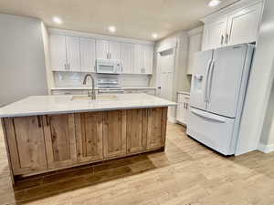 Kitchen with white appliances, white cabinets, light quartz countertops, a kitchen island with sink, and light wood-style tile floors