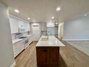 Kitchen with white cabinetry, white appliances, recessed lighting, an island with sink, and light wood style tile flooring