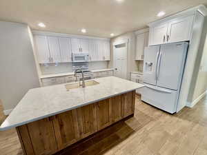 Kitchen with white appliances, white cabinets, light quartz countertops, a kitchen island with sink, and light wood-style tile floors