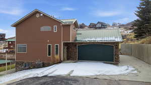Snow covered property with a metal roof and stone siding