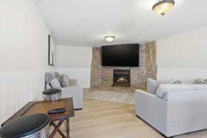 Living room with wood finished floors, a stone fireplace, and a wainscoted wall