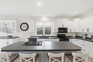 Kitchen with dark countertops, a kitchen bar, white cabinetry, black appliances, and glass insert cabinets