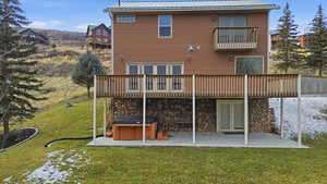 Back of house featuring a hot tub, a lawn, a metal roof, a patio area, and stone siding