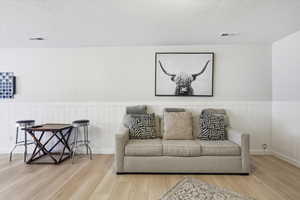 Living area with a textured ceiling, light wood finished floors, and wainscoting