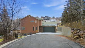 View of property exterior with driveway, a garage, stone siding, and a metal roof