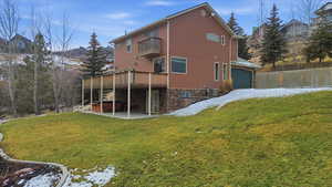 Rear view of property with a hot tub, a patio area, a yard, a garage, and stone siding